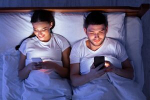 Couple using phones in bed.